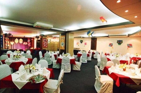 A banquet hall with round tables, white chairs, and red tablecloths.