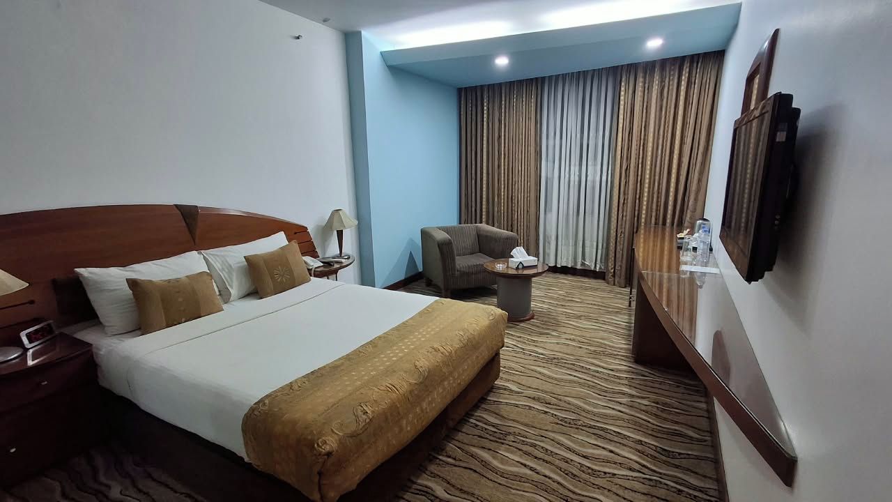 A hotel room with a large bed, a chair, a small table, and a TV mounted on the wall.