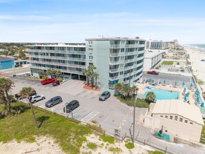 Ein mehrstöckiges Hotel mit Poolbereich, Parkplätzen und Blick auf den Strand.