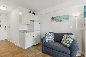 Ein gemütlicher, kleiner Wohnraum mit einer Küchenzeile, einem Sofa mit gemusterten Kissen und einem Bild an der Wand.