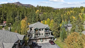 A multi-story building with a balcony, surrounded by dense forest and mountains in the background. - Spacious Breckenridge Townhome, Community Hot Tub (Breckenridge)