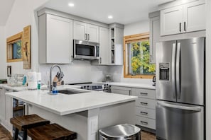 A modern kitchen with white cabinetry, stainless steel appliances, a large island with a sink, and a window with a view of trees. - Spacious Breckenridge Townhome, Community Hot Tub (Breckenridge)