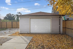A garage with a white door, surrounded by a wooden fence, and covered in fallen leaves. - Emerald Point Family Home - 3BR/2BA with Garage (Chicago)