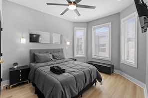 Una camera da letto con un letto, comodini, una ventola a soffitto e ampie finestre.