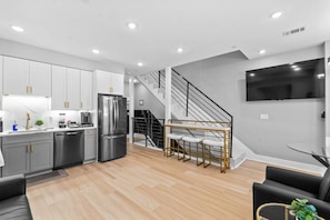 A modern kitchen with stainless steel appliances, a dining area with a staircase, and a flat-screen TV mounted on the wall. - Modern 4BR/3 bath | Rooftop Deck, Parking &Sleeps 12 (Washington)