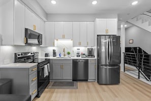 A modern kitchen with stainless steel appliances, grey cabinets, and a wooden floor. - Modern 4BR/3 bath | Rooftop Deck, Parking &Sleeps 12 (Washington)