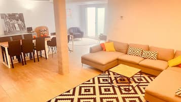 A modern living room with a sofa, a dining area with chairs, and a patterned rug.