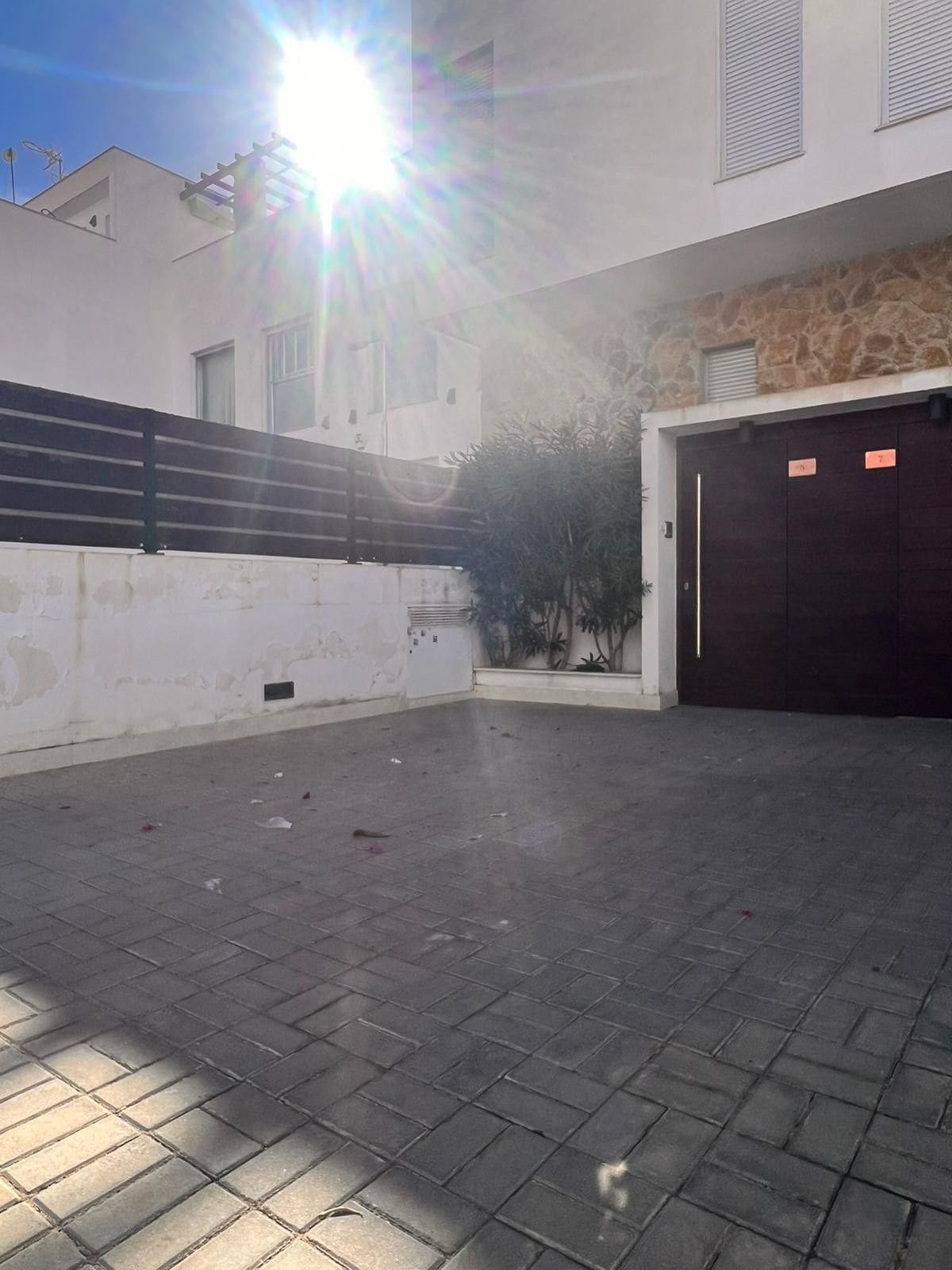 A building with a paved courtyard, a stone wall, and a dark-colored garage door.