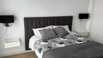 A bedroom with a dark headboard, a bed with patterned bedding, two bedside tables with lamps, and a white bedside drawer.