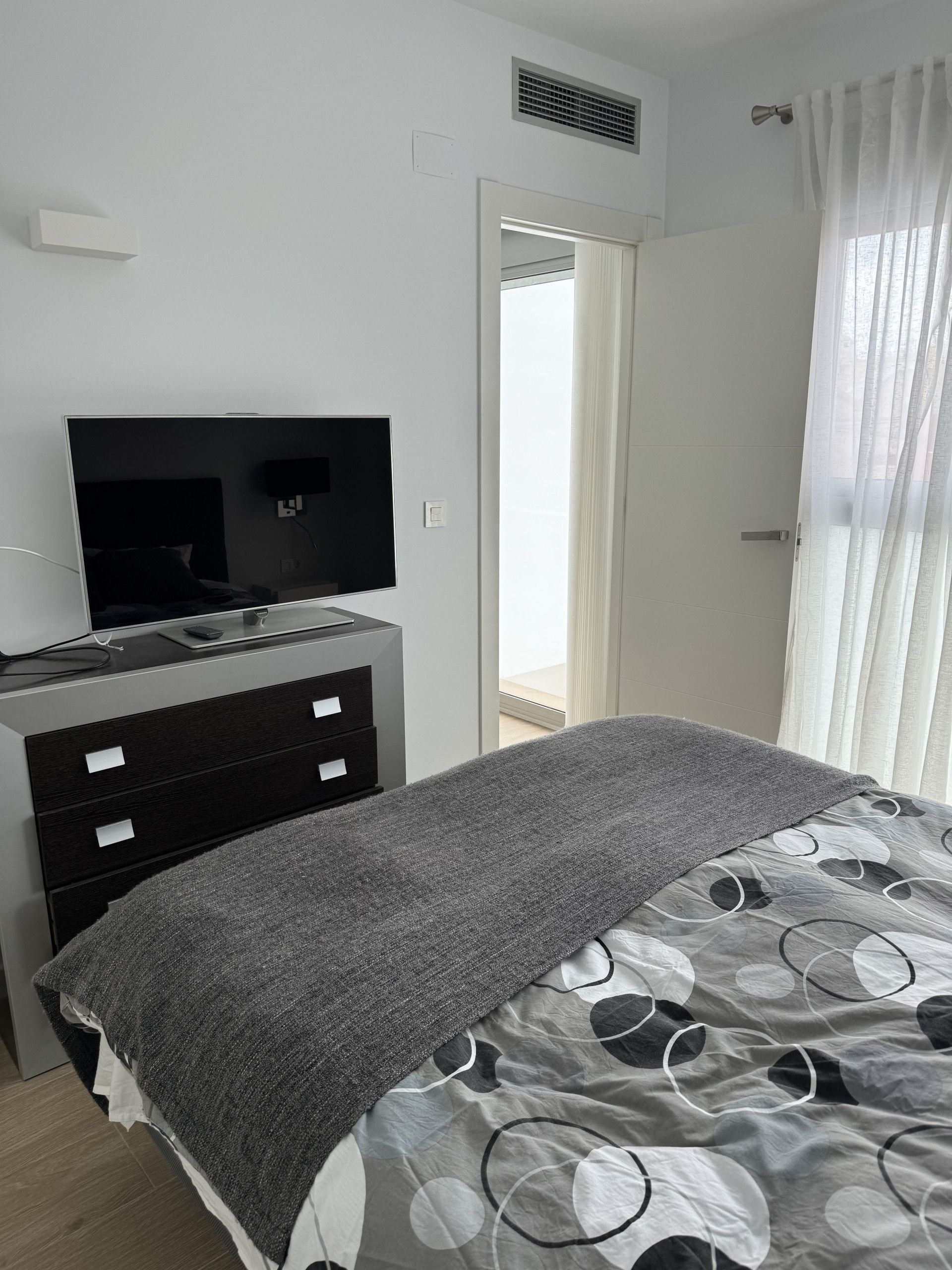 A modern bedroom with a bed, a TV on a dresser, and a view of the outdoors through a door.