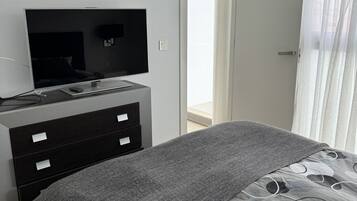 A modern bedroom with a bed, a TV on a dresser, and a view of the outdoors through a door.