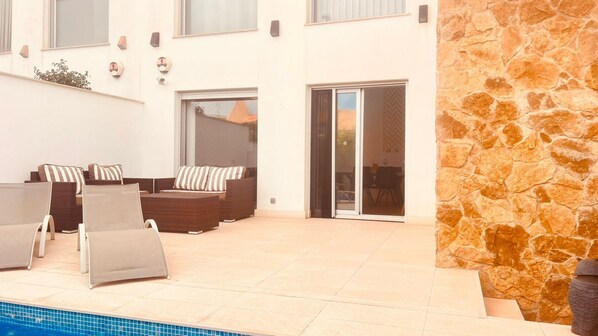 A poolside area with a stone wall, outdoor seating, and a sliding glass door leading to a patio. - Villa With Pool Torrevieja (Torrevieja)