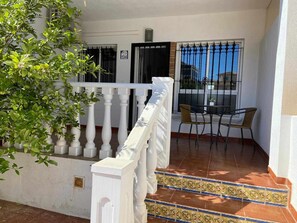 Een balkon met een witte balustrade, betegelde vloer, een tafel met stoelen en een potplant.