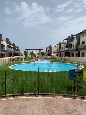 Piscina cercada por uma grade, com edifícios ao fundo.