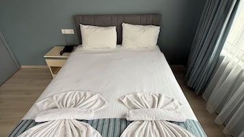 A hotel room with a large bed, two pillows, a bedside table with a lamp, and a wall-mounted light fixture.