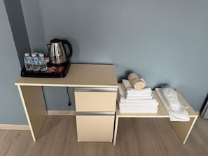A compact room with a desk, a kettle, bottled water, and neatly folded towels.