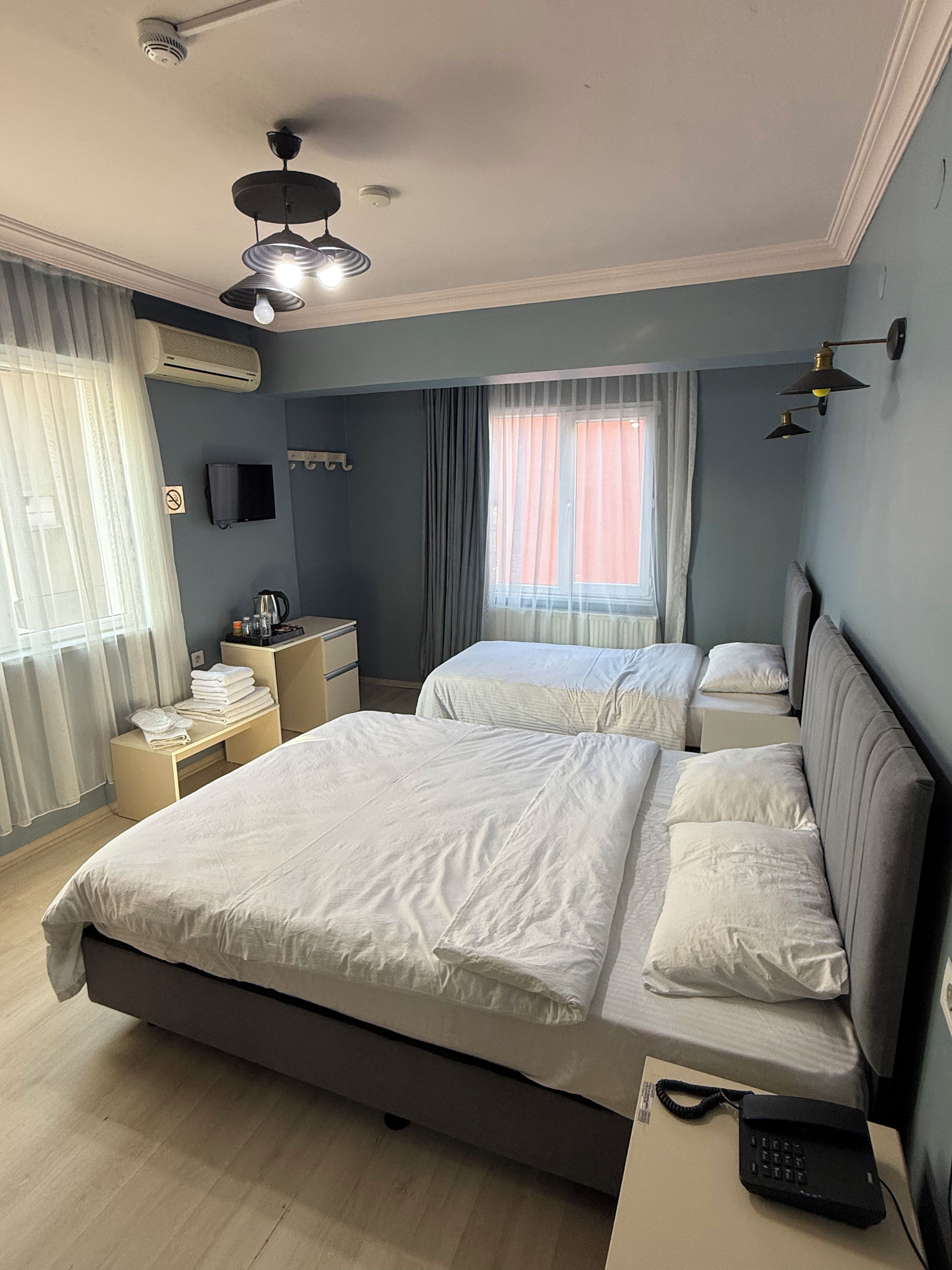 A hotel room with two beds, a desk, a chair, a TV, and a window with curtains.