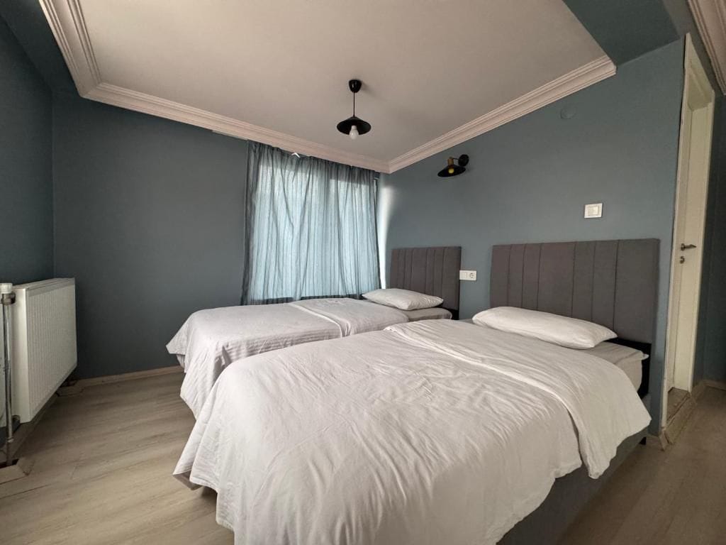A bedroom with two beds, a radiator, and a window with curtains.