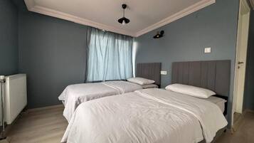 A bedroom with two beds, a radiator, and a window with curtains.