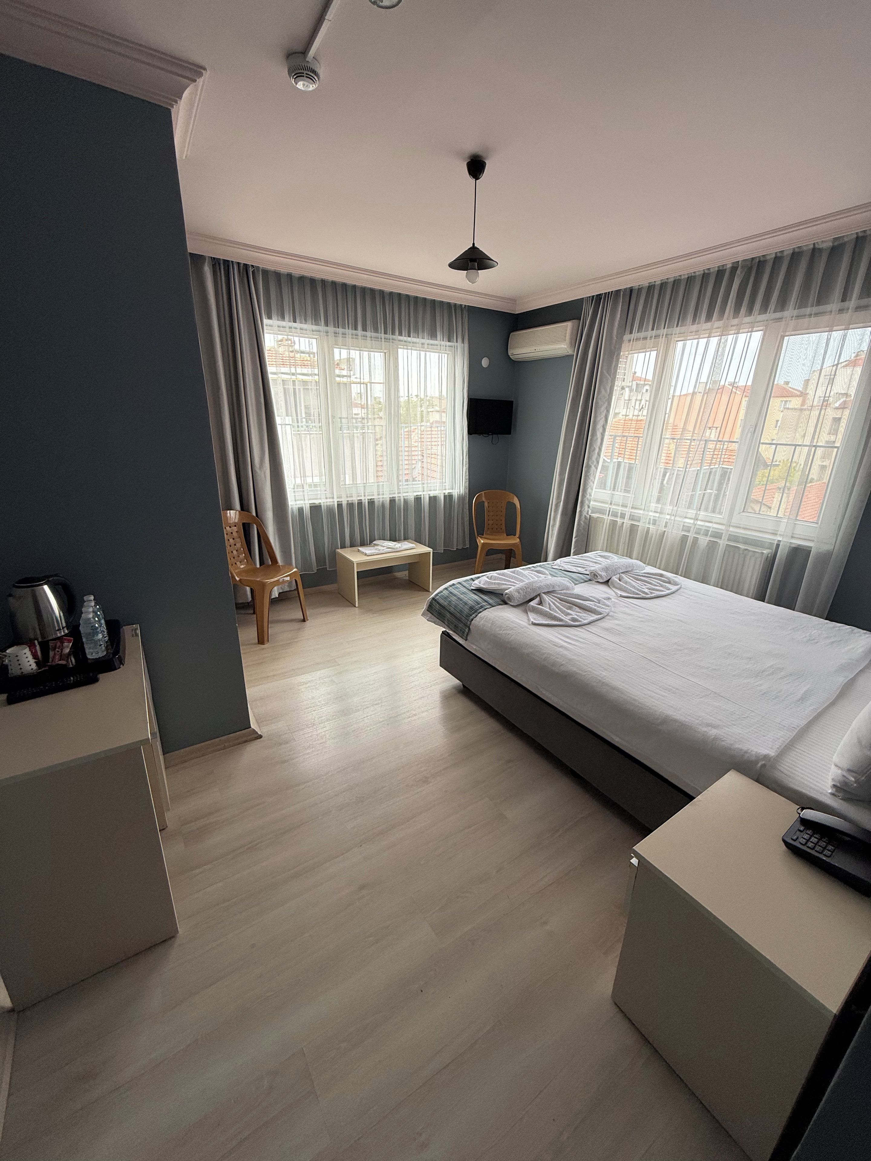 A hotel room with a bed, a desk, a chair, a TV, and large windows with curtains.