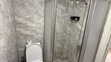A bathroom with a glass-enclosed shower, a toilet, and a marble wall.