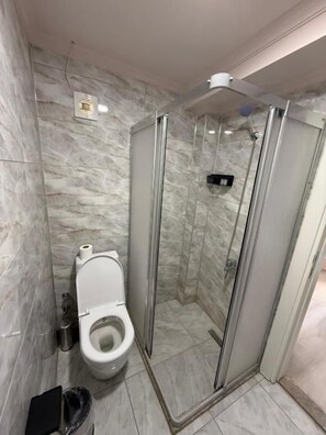 Un baño con ducha de mampara de vidrio, inodoro y pared de mármol.