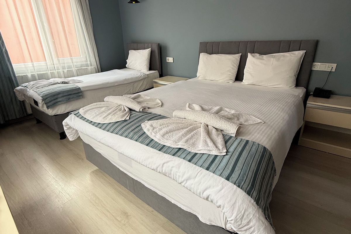 A hotel room with two beds, a large window with sheer curtains, and a wooden floor.
