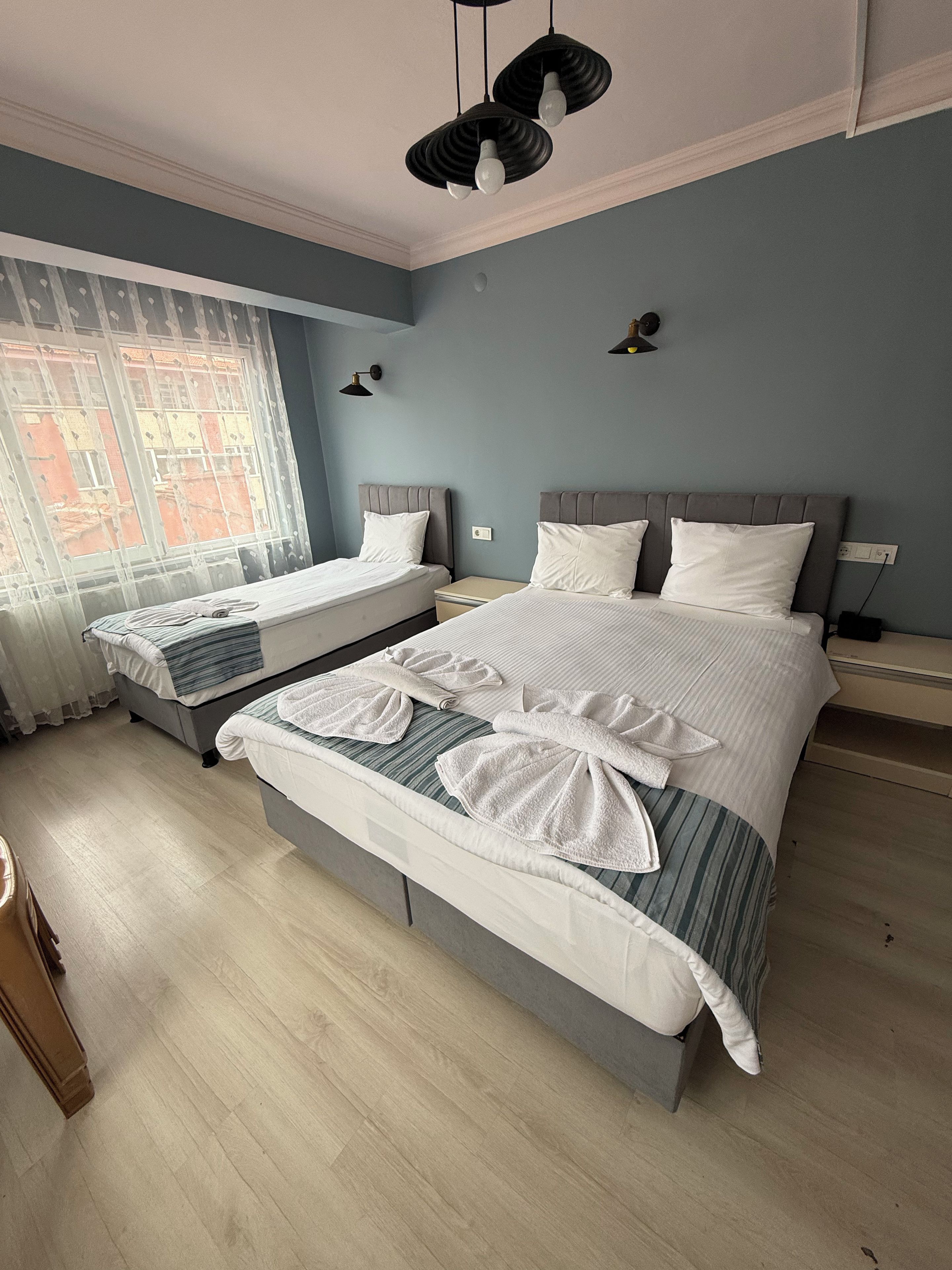 Habitación de hotel con dos camas, un ventanal grande y vistas a un edificio.