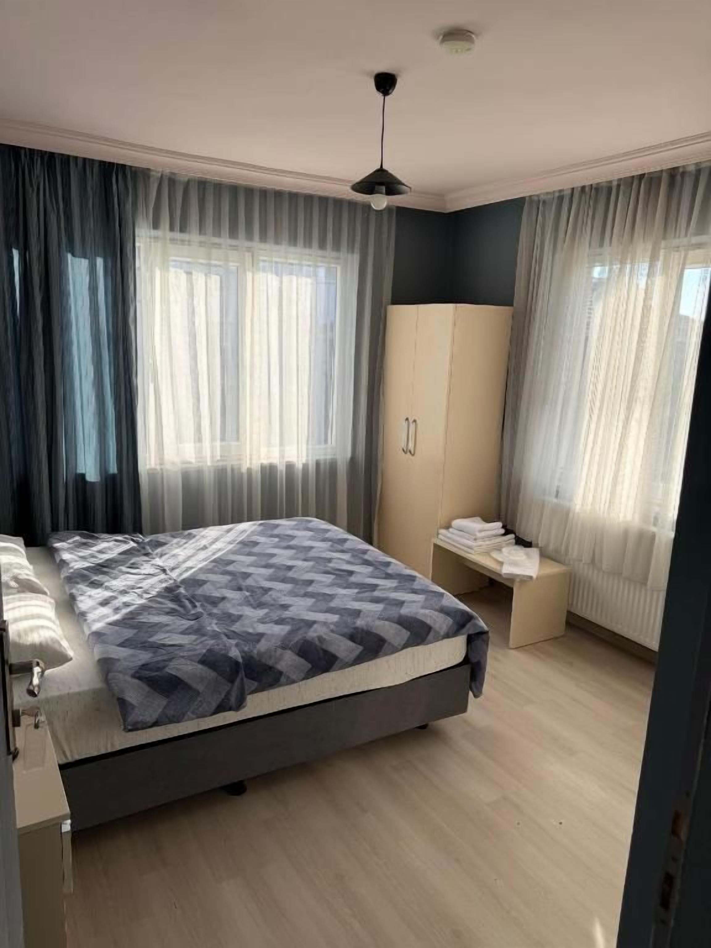 Een slaapkamer met een bed, een kledingkast, een bankje en een raam met gordijnen.