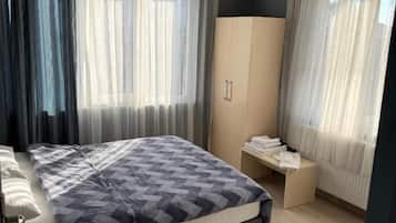 Een slaapkamer met een bed, een kledingkast, een bankje en een raam met gordijnen.