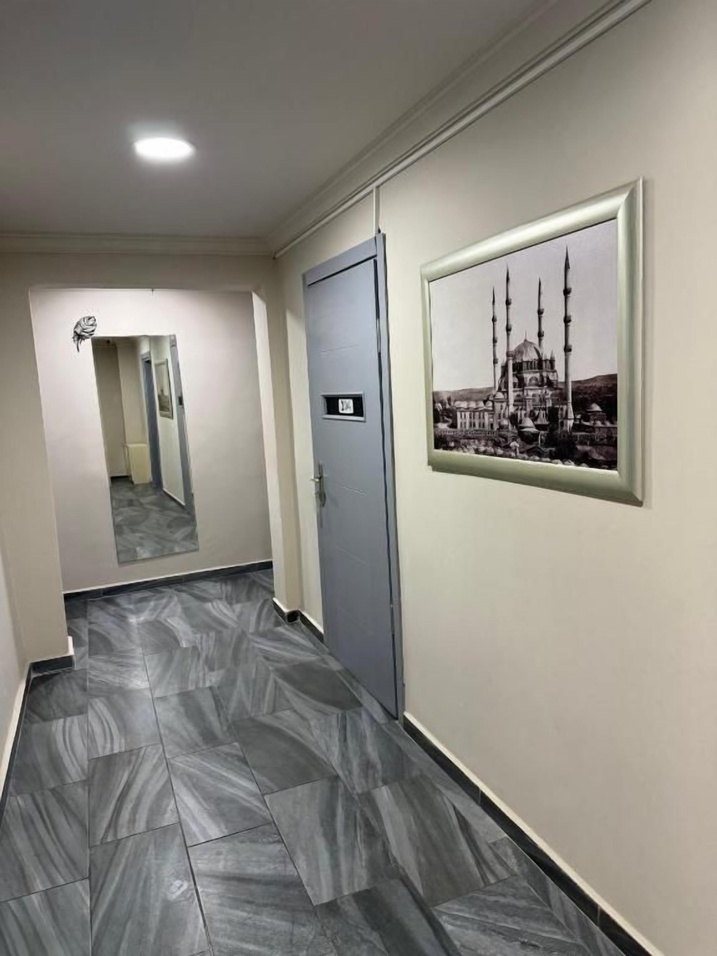 A hallway with a tiled floor, a door with a number, and a framed picture on the wall.