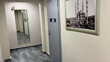 A hallway with a tiled floor, a door with a number, and a framed picture on the wall.