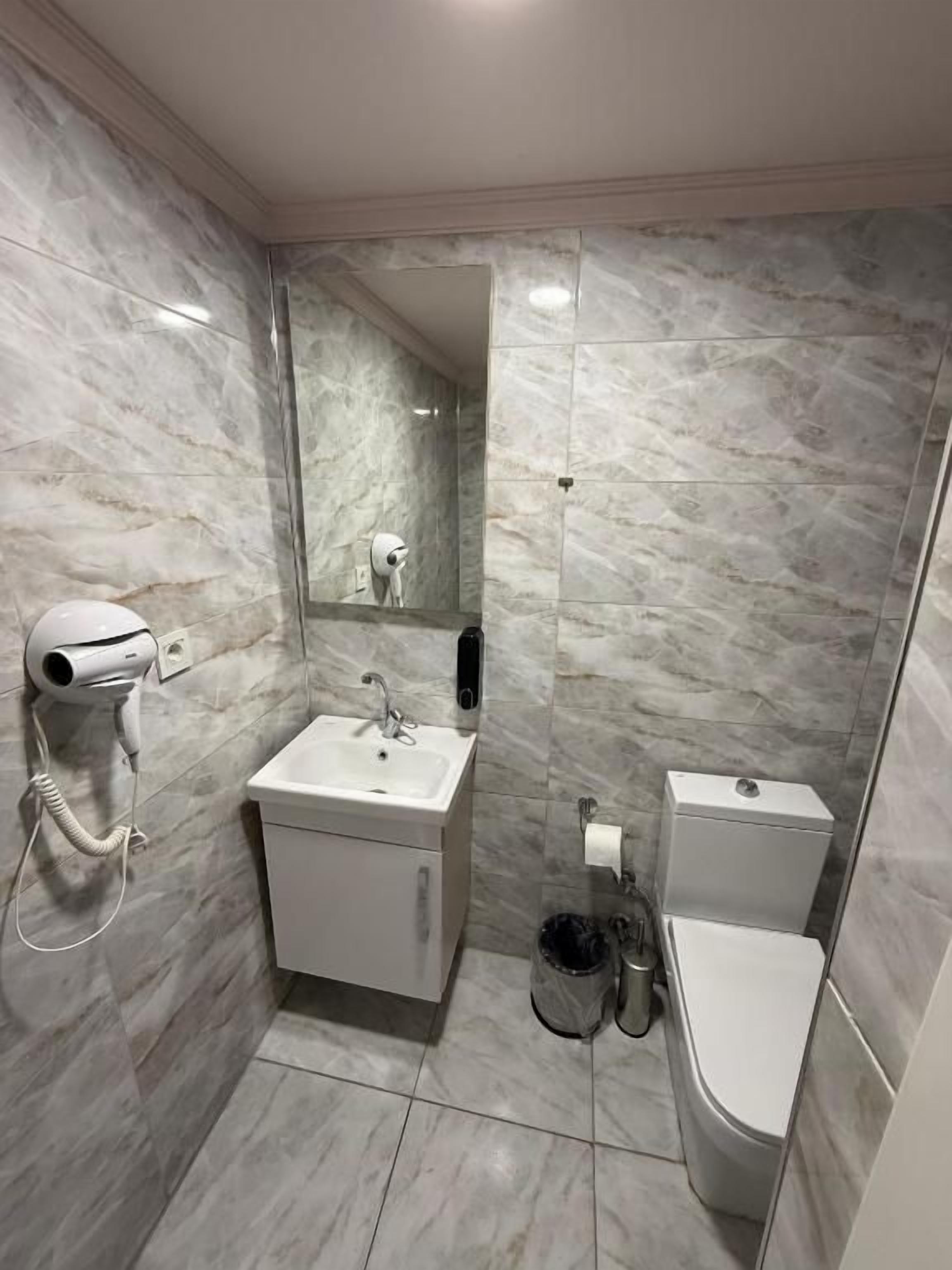 Een badkamer met een marmeren wand, een wastafel, een toilet, een spiegel en een haardroger.