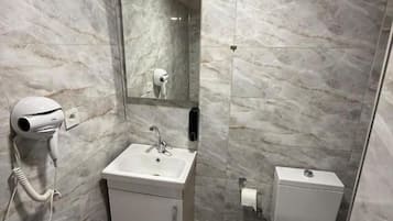 Een badkamer met een marmeren wand, een wastafel, een toilet, een spiegel en een haardroger.