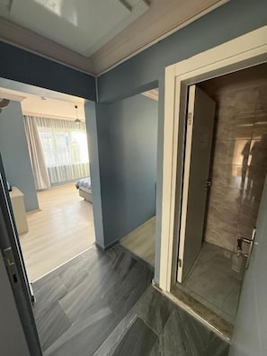 A hallway with a door leading to a bathroom. The hallway has a tiled floor and walls painted in a light color.