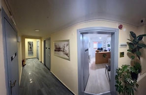 A hallway with a reception desk, framed artwork on the walls, and a potted plant.