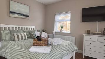 A bedroom with a bed, a dresser, a television, a window with blinds, and a painting on the wall.