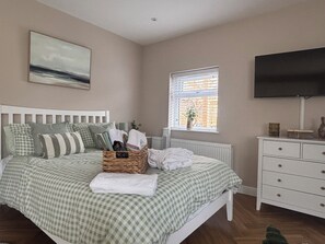 A bedroom with a bed, a dresser, a television, a window with blinds, and a painting on the wall.