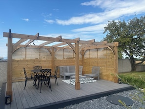 Une pergola en bois avec une table et des chaises, entourée d’une zone recouverte de gravier et d’une terrasse en bois.