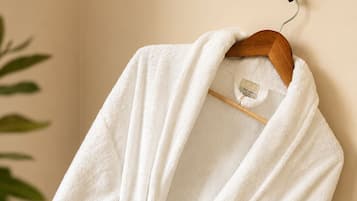 A white bathrobe hanging on a wooden hanger against a beige wall.