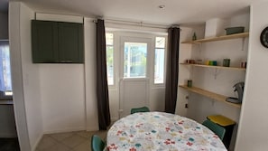 A small room with a table, chairs, a door, and a shelf with various items. - Vacation Rental at Lake Guerlédan (Saint-Aignan)