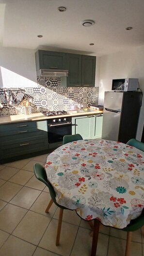 A kitchen with a gas stove, oven, microwave, and a dining table with chairs. - Vacation Rental at Lake Guerlédan (Saint-Aignan)