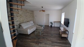 A living room with a stone wall, a sofa, a coffee table, a TV, and a wooden ladder. - Vacation Rental at Lake Guerlédan (Saint-Aignan)