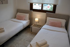 A hotel room with two single beds, a nightstand with a lamp, a window with blinds, and a view of the street outside. - Secreto La Zenia (Orihuela)