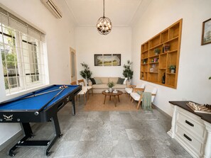 Een woonkamer met een pooltafel, een zithoek, een salontafel en een boekenkast.