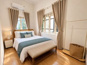 A bedroom with a bed, bedside table, lamp, bench, window, and curtains. - West Lake Peaceful Villa by Anamoi (Hà Nội)