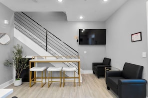 Una sala de estar moderna con una escalera, un televisor de pantalla plana, una zona de comedor con taburetes y dos sofás.