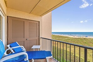 Ein Balkon mit Blick auf den Strand, eine Tür und zwei Liegestühle mit blauen Kissen.