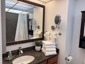 A bathroom with a sink, mirror, towel rack, and a potted plant. - Ocean View Kaanapali Shores Spacious One Bedroom (Lahaina)