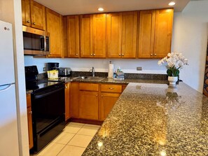 A kitchen with wooden cabinets, a granite countertop, a microwave, a toaster, and a sink. - Ocean View Kaanapali Shores Spacious One Bedroom (Lahaina)
